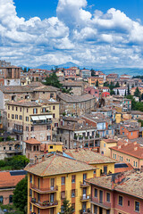 Fototapeta premium Elevated view reveals the tiled roofs of medieval buildings in Perugia, surrounded by lush greenery and distant mountains, embodying the charm of Umbria.