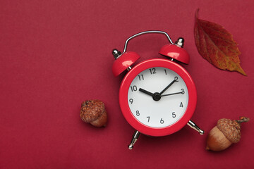 Red alarm clock, acorns and autumn leaves on red background. Daylight saving time end