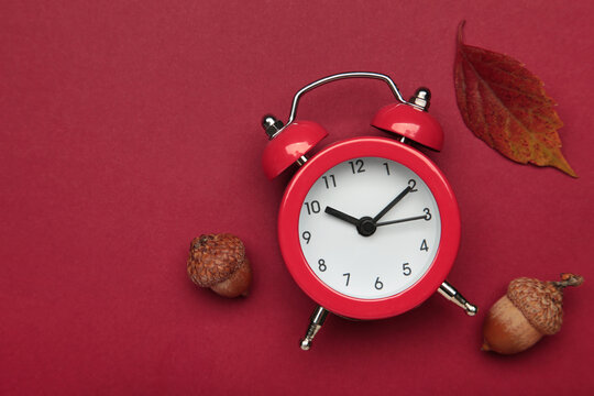 Red alarm clock, acorns and autumn leaves on red background. Daylight saving time end