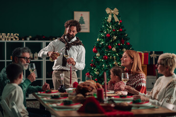 Family celebrating christmas dinner, pouring white wine near christmas tree
