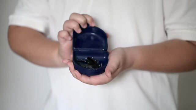 Child opening a blue box with removable dental braces inside. Close-up of hands showing orthodontic retainer case. Dental care and orthodontics concept.
