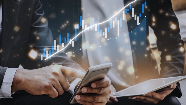 Two business professionals engage with mobile devices, interpreting stock market trends through digital graphs and charts, symbolizing investment strategies and financial analysis. Copula