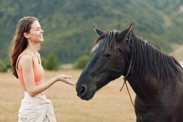 Obraz premium A cheerful woman stands in an open field, reaching out to a horse. She smiles warmly, creating a calm, friendly moment and a gentle connection with nature.