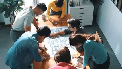 Top view of smart manager writing at blueprint while marketing team plans design. Aerial view of architect engineer working together sharing idea and taking a note in project plan at table. Symposium.