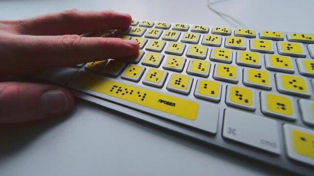 Computer keyboard with braille font alphabet. Blind person is typing words, hands. Technological device for visually impaired people. Tactilely touches bumps on keys. Inclusion, assistive technology