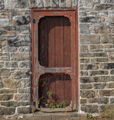 Peeling and faded brown wooden screen door and entry door in a limestone block building, nobody