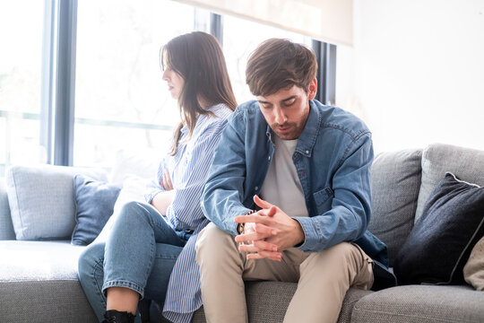 Young couple sitting on sofa at home arguing and confronting each other, concept of relationship problems, breakup, jealousy, betrayal, lack of trust, or communication issues