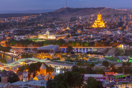 Night view of central Tbilisi, Georgia with illuminated landmarks including Holy Trinity Cathedral and Bridge of Peace
