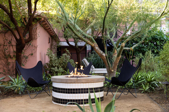 Firepit with fire in a garden with black butterfly chairs and surrounded by trees
