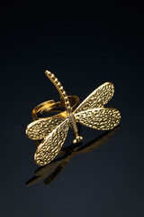 Yellow metal dragonfly ring on black glass with reflection