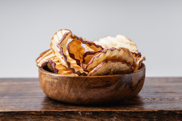 Apple dry slices in a wooden bowl on a light gray background.