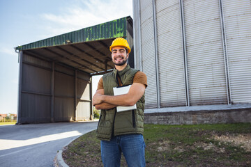 Young worker standing in front of silo holding tablet