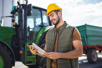 Young worker standing in front of tractor holding tablet