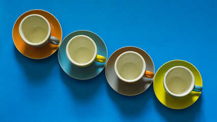 Top view of a colorful set of porcelain cups and saucers arranged diagonally, on a blue background.