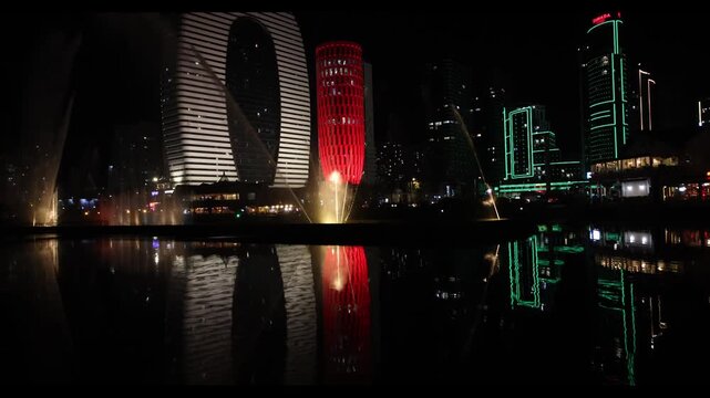Night panorama of the city of Batumi. Hotels, skyscrapers and apartments located near the singing fountain. Reflections of buildings in the water