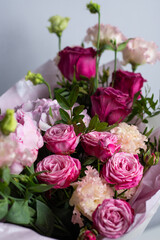 Pink bouquet of roses, peonies, eustoma and hydrangea on a light background. Festive professional flower arrangement in soft pink tissue paper. Romantic bouquet of buds and greenery close-up