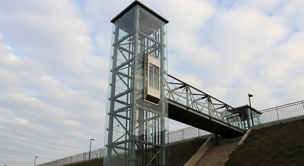 Modern glass elevator tower with bridge against cloudy sky