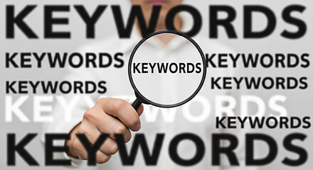 Person holding magnifying glass over the word keywords for search engine optimization and online marketing strategies to improve website visibility