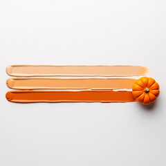 Creative flat lay of cosmetic swatches in a warm autumn color palette. Foundation or concealer smears with a mini pumpkin on a white background. Beauty concept for Halloween and seasonal makeup.