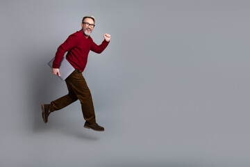 Obraz premium Handsome businessman holding a laptop in a red sweater mid-stride on a light gray background, exemplifying confidence and success