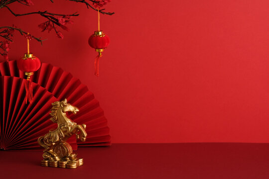 Golden horse figurine on coins with red lanterns and paper fans. Symbol of prosperity and strength in festive Chinese New Year 2026 setting.