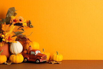 Red toy truck with pumpkins and fall foliage on brown surface on orange background. Autumn, fall, Thanksgiving concept.