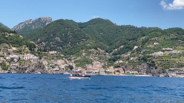 View from boat on amazing hills with colourful houses along the Amalfi coast, exploration journey and summer vacation in Italy, rock cliffs with hidden caves for tourist destination, famous towns and