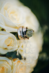 Wedding rings resting on a bouquet of white roses and eucalyptus. Symbol of love, fidelity, and celebration. Elegant floral composition in natural light.