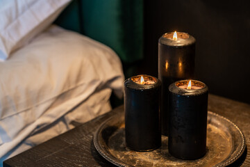 Black candles burning flame on silver platter beside bed on nightstand