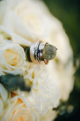 Wedding rings resting on a bouquet of white roses and eucalyptus. Symbol of love, fidelity, and celebration. Elegant floral composition in natural light.