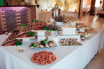 Buffet table with assorted appetizers and snacks at a festive event. Elegant catering setup with meat platters, canapés, and decorated dishes. Wedding or banquet celebration concept.