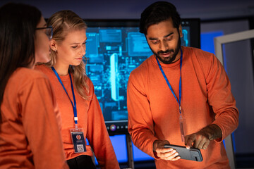 Diverse IT expert collaborate on a digital project in a blue-lit data center. A male developer shows critical information on a mobile device. technological consultation and teamwork.