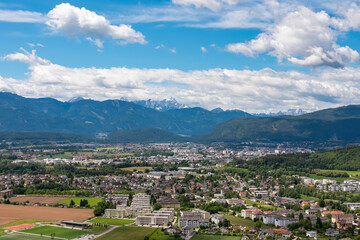 Obraz premium A stunning panoramic view of a city in Carinthia, Austria, nestled in green valley under blue sky, with the snow-capped Karawanks mountain range dominating the scenic alpine background from Landskron