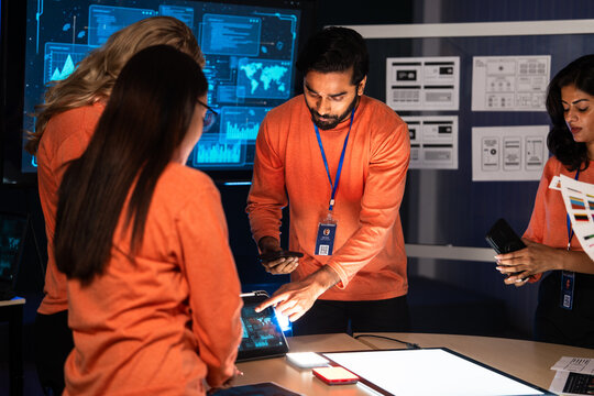 A diverse team of software engineers and UX,UI designers collaborates on a new mobile device. They are brainstorming a cybersecurity project, hardware, software or new technology launch