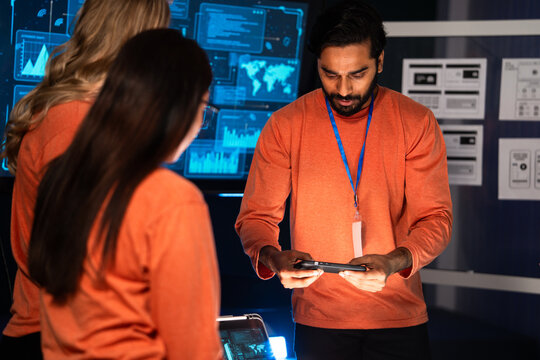 A diverse team of mobile app developers meeting and brainstorming new software or hardware product. They are reviewing critical data and security protocols on digital devices cybersecurity