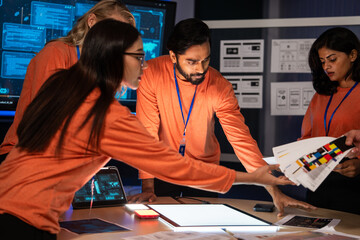A diverse creative team is collaborating in a control center. Reviewing UI, UX wireframes and color palettes to solve a critical design problem for a new product. Project meeting and brainstorming