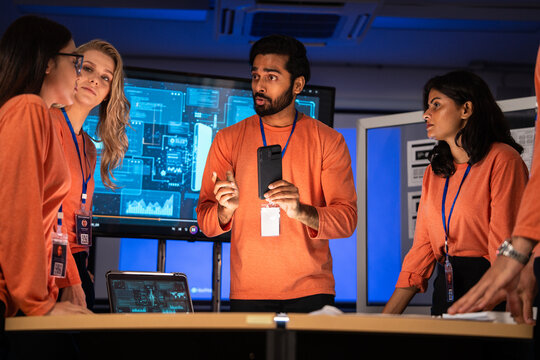 Expert cybersecurity team strategizing in a high-tech control room. Indian IT presenting a smartphone while discussing a critical data problem. Focus on digital security, tech solutions, and teamwork
