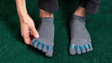 Wearing blue toe spacers over gray socks for bunion prevention and foot alignment, adjusting silicone toe separators for natural toe splay and orthopedic support on green carpet