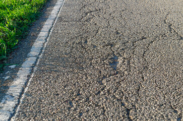 German Road Cracks in Late Sunlight; Cracked road with road marking and roadside greenery close-up