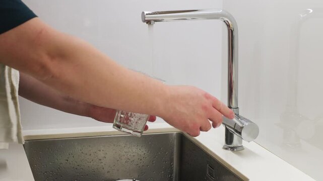 Filling Glass with Tap Water at Kitchen Sink &mdash; Close-Up of Hands Turning Chrome Faucet