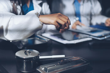Two doctors and a female nurse meet at a table in the hospital, collaborating on medical tasks using laptops and computers