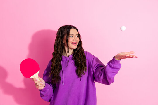 Young woman in casual sweatshirt holding a ping pong paddle, posing with a smile against a vibrant pink backdrop - Powered by Adobe