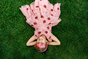 A girl with glasses is lying on the grass. A cheerful child is playing and laughing in the park.