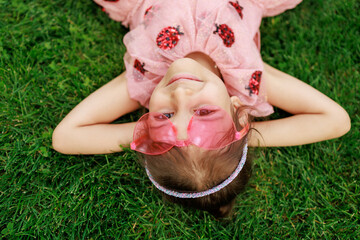 A girl with glasses is lying on the grass. A cheerful child is playing and laughing in the park.