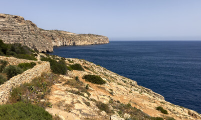 Malta's rugged limestone cliffs plunge into the deep blue Mediterranean, framed by ancient dry-stone walls.