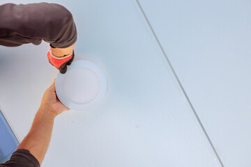 Worker wearing gloves is placing round light fixture onto ceiling