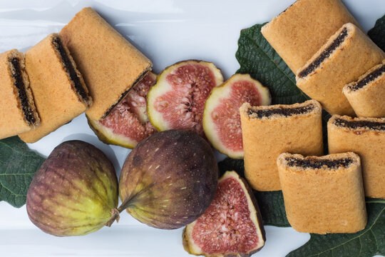 Fig bars and two fresh juicy figs and sliced figs with fig leaves on white serving plate. High quality photo