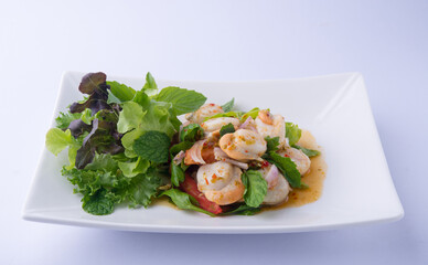 Spicy Scallop Salad, a Thai dish. Large orange scallops tossed in a dressing, mint, basil, and salad greens on a white plate.