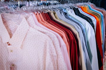 A colorful rack of men's dress shirts neatly hung on transparent hangers, featuring a range of soft pastels, bold hues, and subtle patterns in a fashion store.
