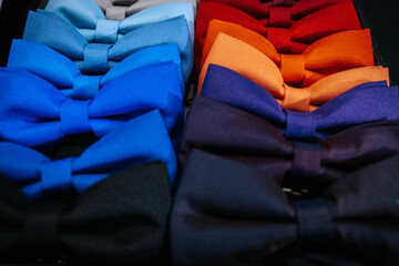 Fototapeta premium A colorful display of bow ties arranged by hue, featuring shades of blue, gray, red, pink, yellow, and burgundy, neatly stacked in a retail fashion store.